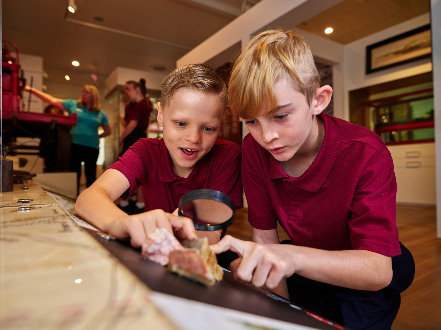 two boys looking at rocks and gems through a magnifying glass as part of a permanent display