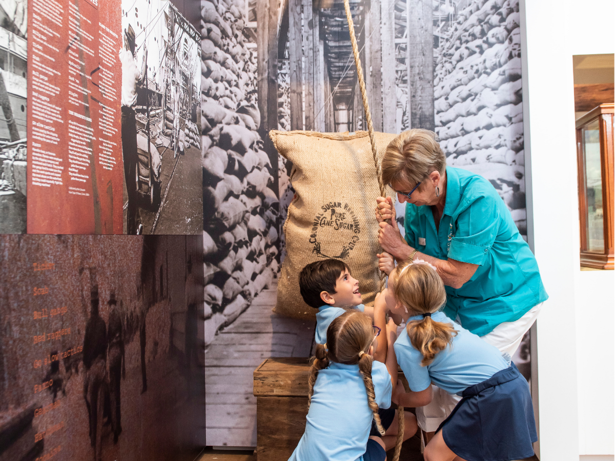 Children and Museum guide pulling on a rope to lift bag of wool that is part of interactive display